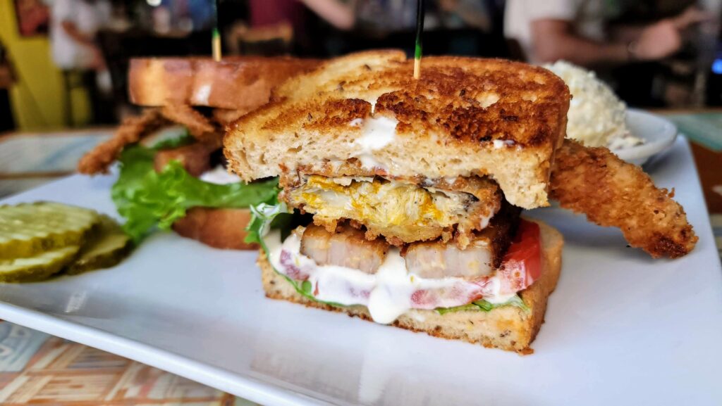 The Crabby Pig Sandwich – It’s made with lettuce, tomato, thickly sliced pork belly, a crispy fried soft-shell crab, and dressed with a cilantro lime sauce, all served on toasted rye bread served at Riverside Cafe in Vero Beach, Florida.