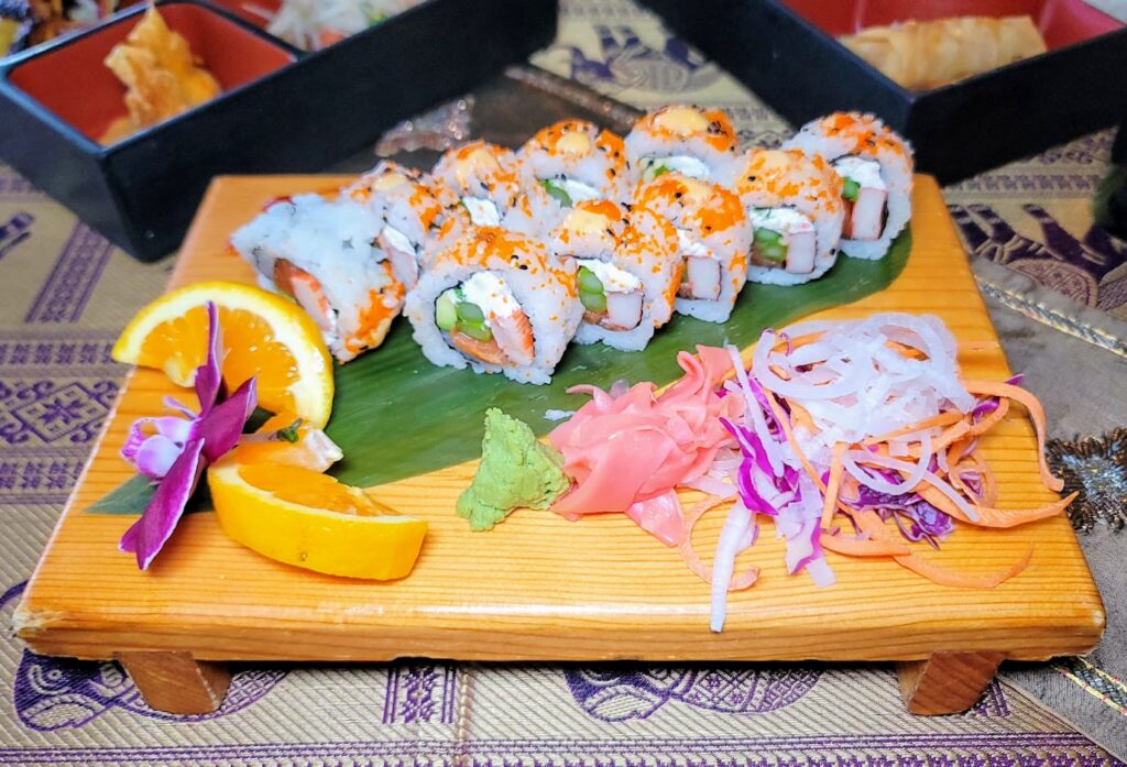 Sushi roll served on a raised lightly stained wood board, and served with orange slices, wasabi, ginger, onions, carrots & purple cabbage slaw at Thai Esan Zabb in Vero Beach florida