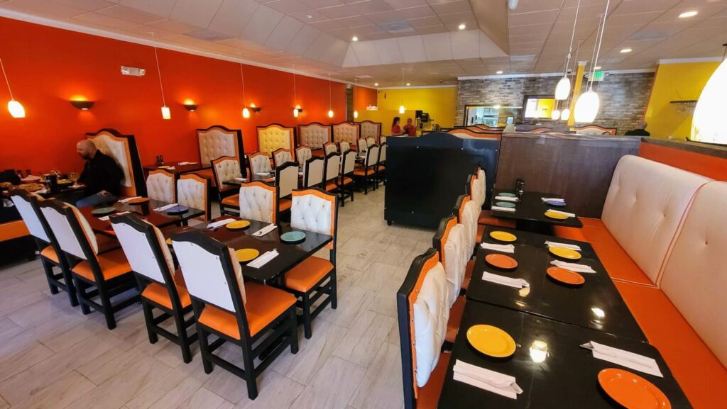 The dining room at Casa Amigos Mexican Restaurant in Vero Beach, Florida features orange and yellow walls, padded chairs and booths, and black tables. Located in the Miracle Mile shopping district, the atmosphere is cozy and inviting, perfect for enjoying delicious Mexican cuisine.