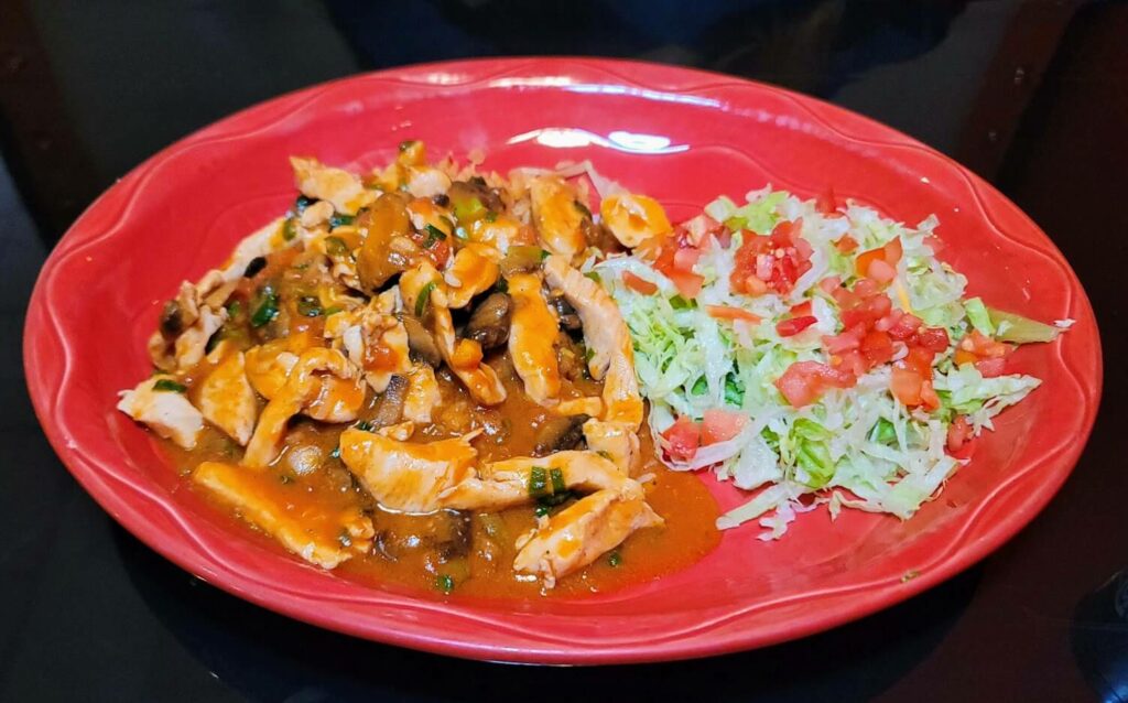 "A delicious plate of Arroz Con Pollo, made with a creamy cheese sauce, poblano peppers, and tomatoes, served over a bed of rice, accompanied by a side of fresh lettuce and tomatoes, at the Tequila Azteca restaurant in vero beach florida
