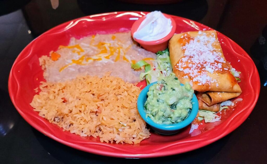 "A hearty plate of a fried ground beef chimichanga, served with a side of guacamole, sour cream, beans and rice, at the Tequila Azteca restaurant in vero beach florida.