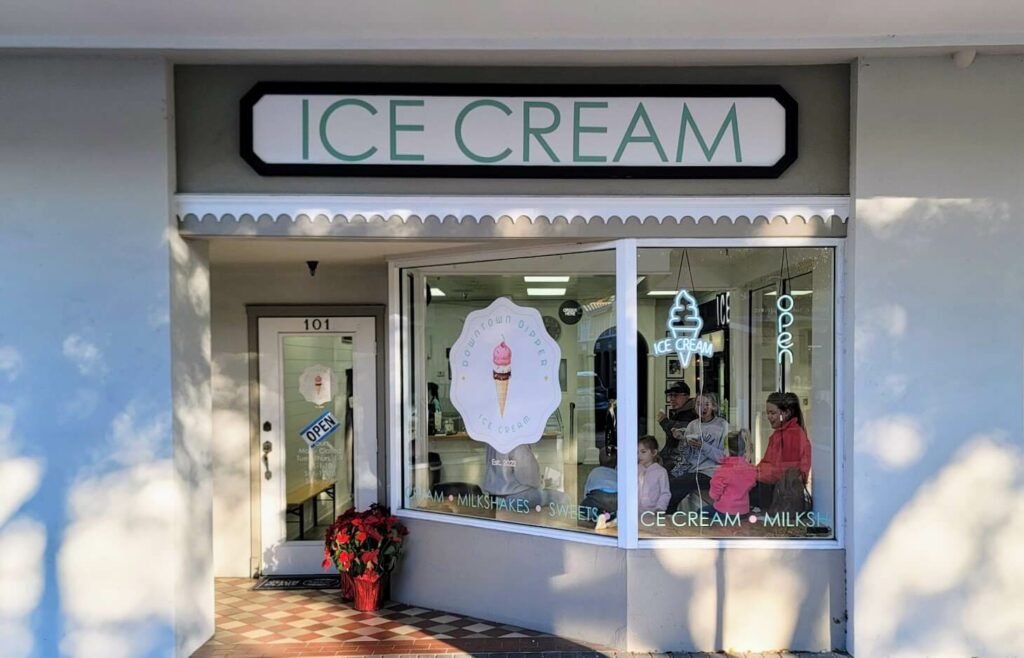 Front exterior of the downtown Dipper ice cream shop in Vero Beach, Florida, featuring a white scalloped awning and display window showcasing various flavors of ice cream.
