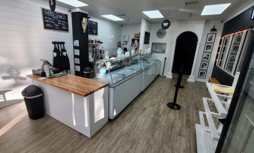 A quaint ice cream shop with white walls and black accents, featuring an ice cream case displaying 24 different flavors.