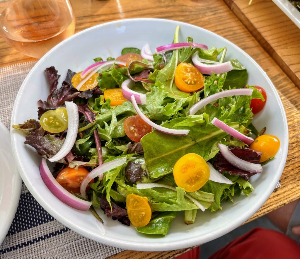 A beautiful plate of mixed greens salad with cherry tomatoes, red onions, and mixed greens dressed and served with a delicious vinaigrette dressing