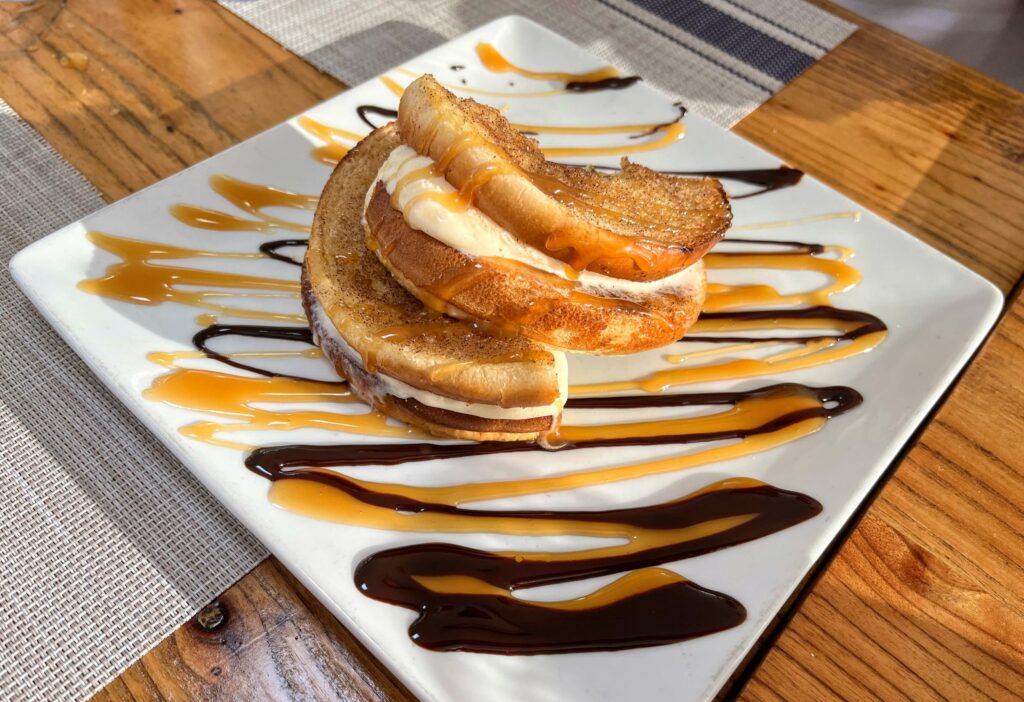 A delicious dessert of a Cinnamon Toasted Ice Cream Sandwich drizzled with caramel sauce, served warm, perfect to finish a delicious meal, with a scoop of vanilla ice cream sandwiched between two slices of cinnamon toast, perfect for a sweet tooth