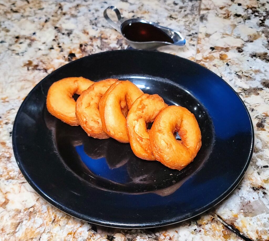 a black plate with 5 cake donuts and a side of honey in a gravy boat served at Ceviche 28, a Peruvian restaurant located in Vero beach, Florida
