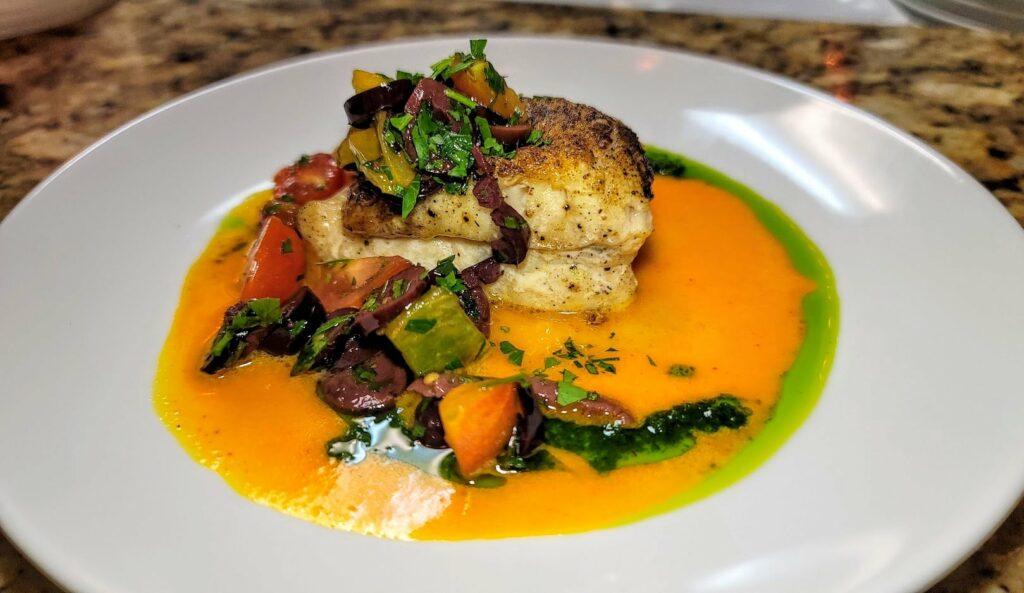 Pan seared golden seabass served with an olive relish, tomatoes, saffron vinaigrette, and fresh herb oil at Fire and Wine on Oslo Road in Vero Beach, Florida.