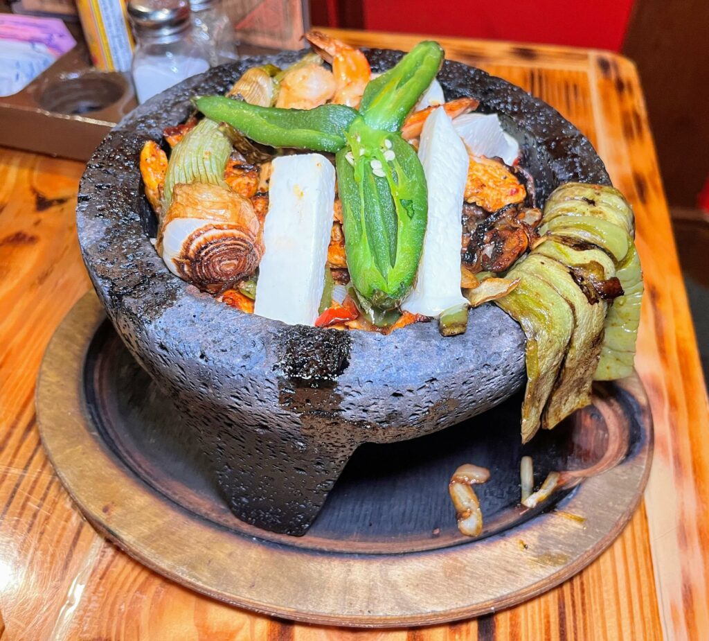 Trio Molcajete - A molcajete is a stone tool, the Mexican version of a mortar and pestle, used for grinding various foods. Steak, chicken, and shrimp cooked with bell pepper, onion, tomato, chorizo, queso, and jalapeño at El Rey Mexican restaurant in vero beach florida.