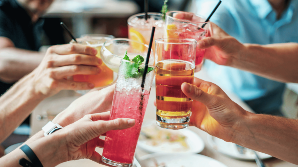 Close Up of people's hands clinking colorful cocktails in a celebratory toast at a restaurant.