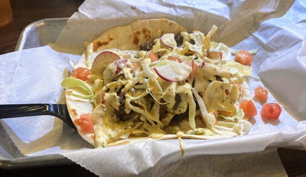 One steak taco with shredded cabbage, diced tomato, radish, queso fresco, and signature dive sauce from taco dive downtown fort pierce location on the treasure coast of florida