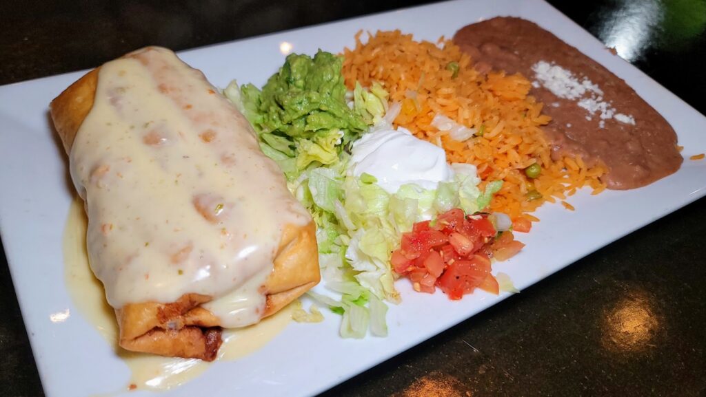 chimichanga covered in cheese queso sauce, guacamole, sour cream, diced tomatoes, rice & beans as prepared by el rey mexican restaurant located in vero beach florida 