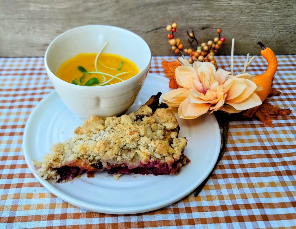 A cup of pumpkin soup and a white and red plum tart with fall decor as prepared by A Kitchen of Her Own, also known as AKOHO located in Sebastian florida