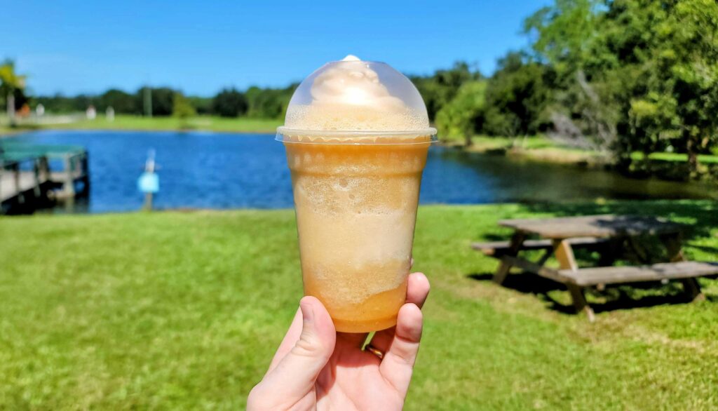 a photo of an apple pie slushie taken outside in tront of a picnic table with a pond in the background at Countryside Family Farms located in vero beach florida