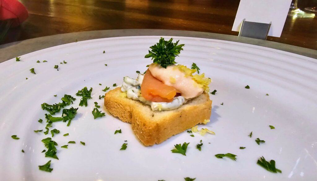 Amuse-Bouche - Smoked salmon bite on crostini, with fresh grated lemon and parsley as served at a supper club dinner at the Sun Market Sauce Co. in Vero Beach Florida